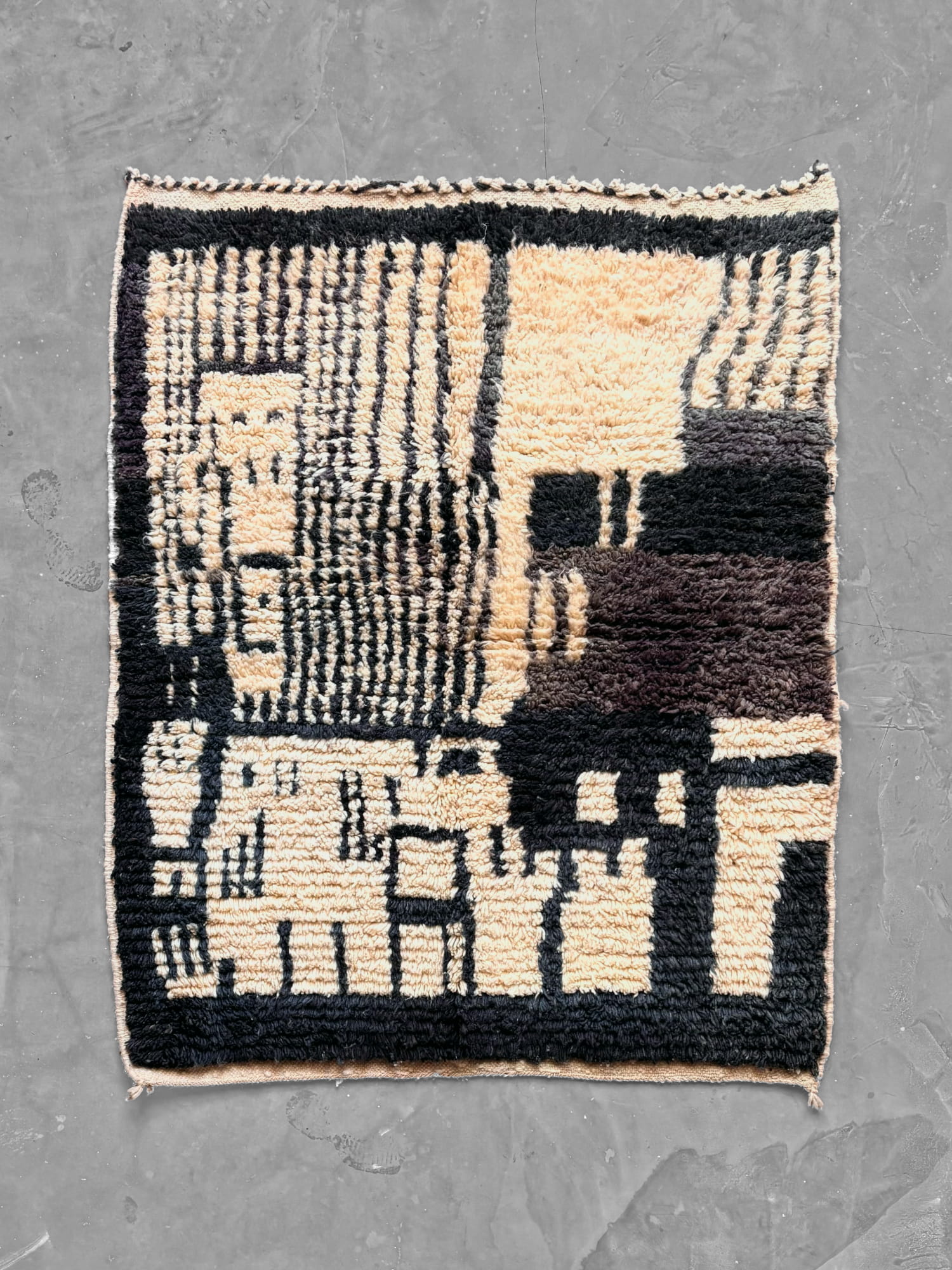Alfombra marroquí Boujad de lana en negro y crema, con detalles en marrón chocolate, de diseño abstracto con rayas y bloques geométricos y cenefa negra. Vista general desde arriba.