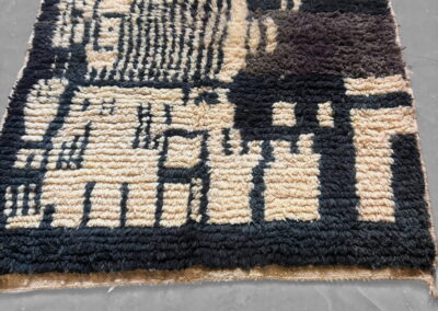 Alfombra marroquí Boujad en negro y crema con detalles en marrón chocolate. Vista general en perspectiva del dibujo abstracto de rayas y bloques geométricos con cenefa negra.