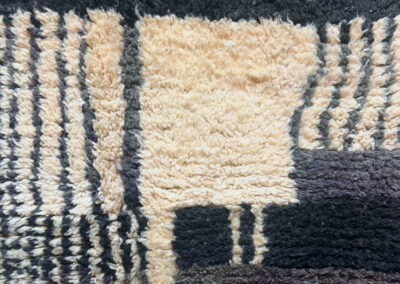 Detalle de alfombra marroquí Boujad en crema, negro y marrón chocolate. Cordón trenzado del borde superior, rayas verticales y bloques de pelo largo.