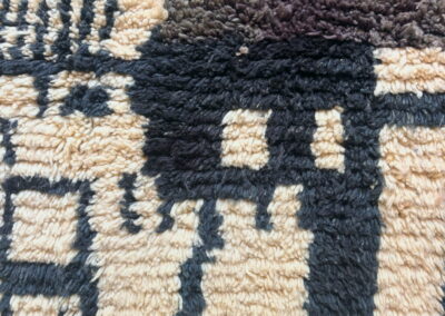 Detalle de alfombra marroquí Boujad en crema, negro y marrón chocolate. Primer plano de los bloques geométricos y del pelo largo de lana.