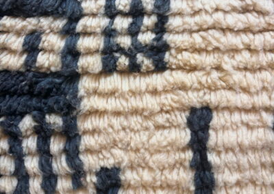 Detalle de alfombra marroquí Boujad en crema y negro. Primer plano de la lana de pelo largo, con motivos lineales en negro sobre fondo crema.