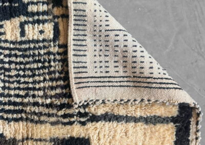 Detalle de alfombra marroquí Boujad en negro y crema. Esquina doblada que enseña el reverso tejido a mano, con su dibujo de pequeñas rayas.