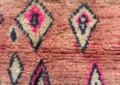 Alfombra marroquí Boujad New Works: rombos en crudo, fucsia y gris antracita sobre campo rosa salmón, junto a los flecos anudados. Detalle.
