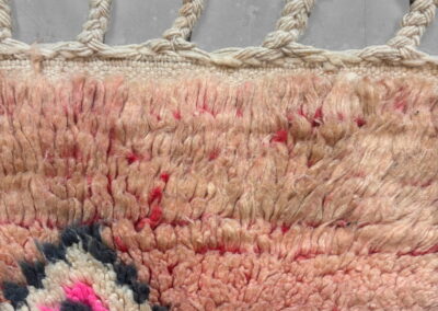 Alfombra marroquí Boujad New Works: extremo con flecos trenzados y anudados, remate de kilim crudo y pelo largo rosa salmón. Detalle.