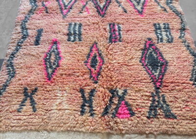 Alfombra marroquí Boujad New Works rosa salmón con rombos fucsia, antracita y crudo, zigzags laterales y kilim crudo. Vista general en perspectiva.