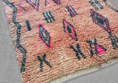 Alfombra marroquí Boujad New Works rosa salmón con rombos, rayas y aspas en antracita y fucsia. Vista general en perspectiva lateral.