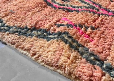 Alfombra marroquí Boujad New Works: borde en perspectiva con zigzag gris antracita y rombos fucsia sobre lana rosa salmón. Detalle.