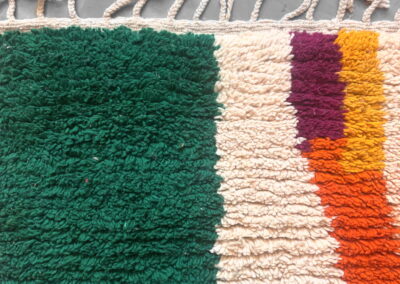 Detalle de los flecos anudados a mano y del borde superior de una alfombra Boujad nueva en verde, crema y naranja