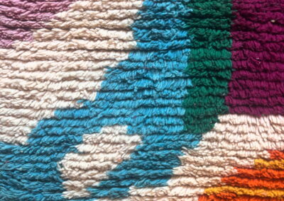 Detalle del pelo largo de una alfombra Boujad nueva en turquesa, verde, ciruela, rosa y naranja sobre fondo crema