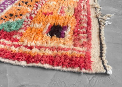 Boujad New Works Moroccan rug: corner in perspective with red border, ecru kilim end and knotted tassel. Detail.