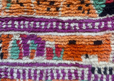 Boujad New Works Moroccan rug: orange and fuchsia bands with sea green and black signs, seen from above. Detail.