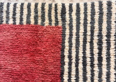 Detalle de alfombra Boujad, esquina con bloque rojo, rayas gris antracita y crema y flecos con borlas