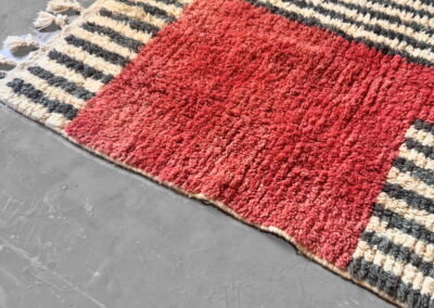 Detalle en perspectiva de alfombra Boujad, bloque rojo, rayas y flecos con borlas